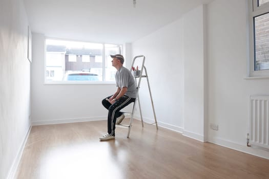 man sitting on ladder looking at newly decorated white painted room