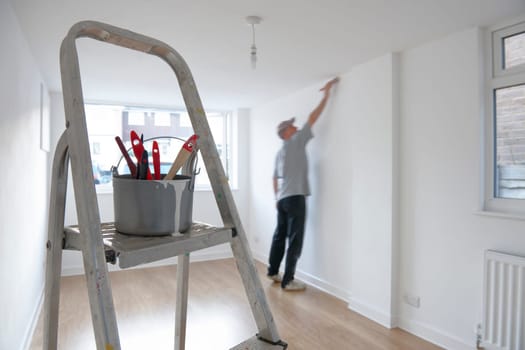 man decorating a room with ladder and paint pot in foreground