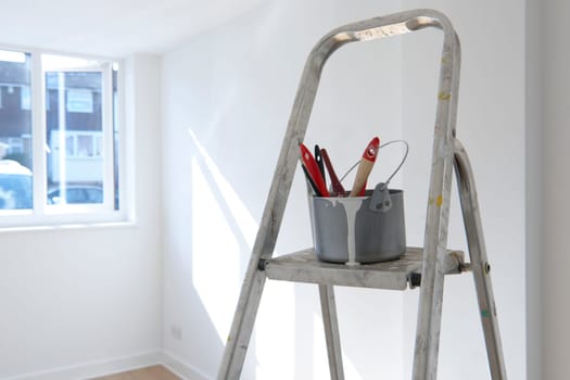 ladder with paint pot and brushes standing in empty room