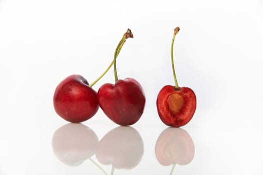 studio shot of red cherries on white background with one cut in halve