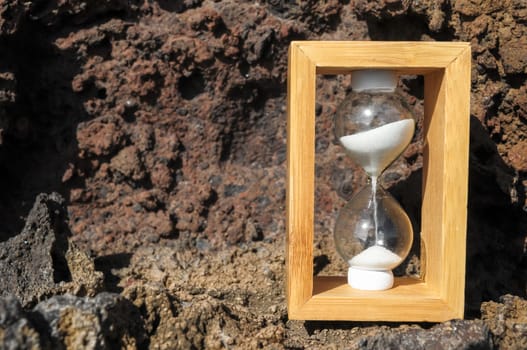 Time Concept White Sand Hourglass on the Volcanic Rocks