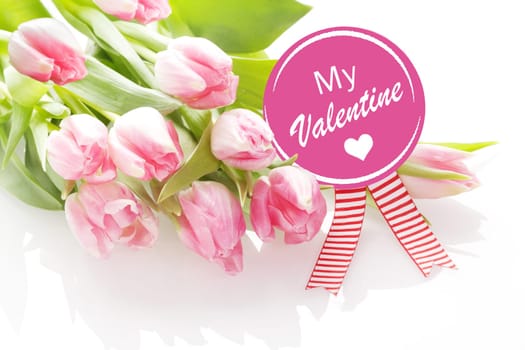 My Valentine greeting card with a bunch of fresh pink tulips lying on a white background with a round pink rosette with a festive striped ribbon and message - My Valentine - with a heart