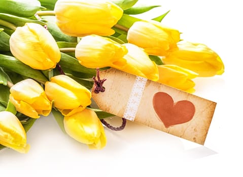 Vintage aged paper label with a red heart on a bunch of pretty fresh yellow tulips over a white background