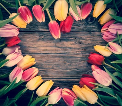Empty colourful heart-shaped frame of fresh tulips arranged on an old rustic wooden background with central copyspace for your Valentines, engagement, of anniversary message to a loved one