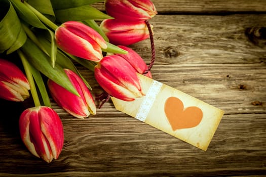 Bouquet of red tulips with a vintage red heart gift tag lying on rustic weathered wooden boards, closeup overhead view with copyspace for a loving message on Valentines Day or an anniversary