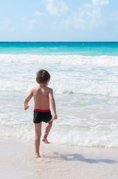 Blond boy runs into the turquoise sea in the Caribbean.