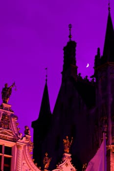 Towers and façade of Bruges Town Hall in the moonlight in radiant orchid