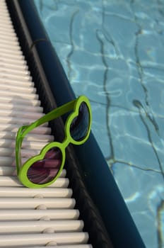 Green sunglasses with heart shapes on a swimming pool