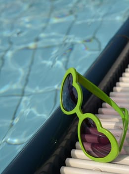 Green sunglasses with heart shapes on a swimming pool