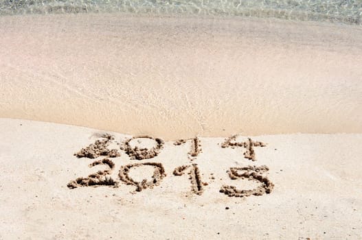 New Year 2015 is coming concept - inscription 2014 and 2015 on a beach sand, the wave is starting to cover the digits 2014