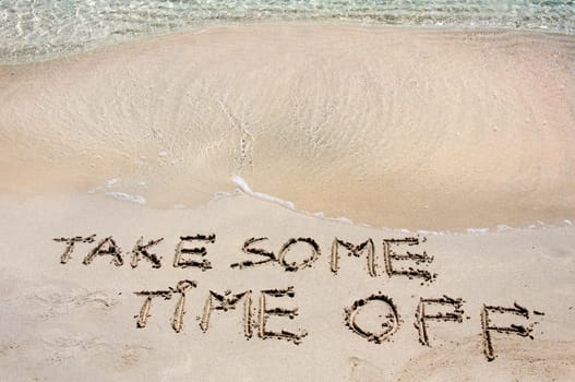 TAKE SOME TIME OFF written on sand on a beautiful beach, blue waves in background