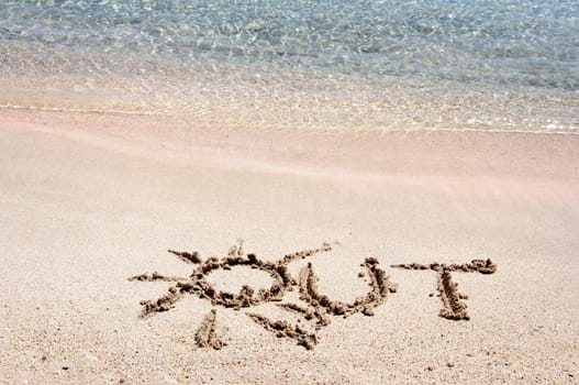 Word "OUT"" written on sand on a beautiful beach, blue waves in background"
