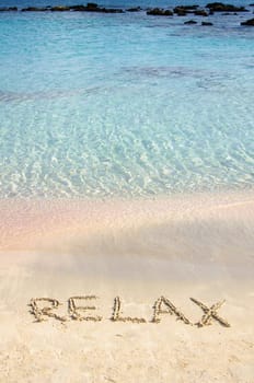 Relax word written in the sand, on a beautiful beach with clear blue waves in  background