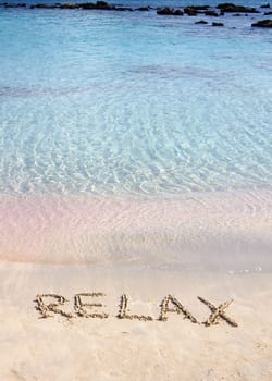 Relax word written in the sand, on a beautiful beach with clear blue waves in  background
