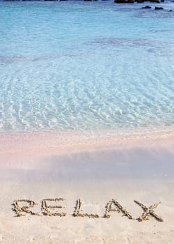 Relax word written in the sand, on a beautiful beach with clear blue waves in  background