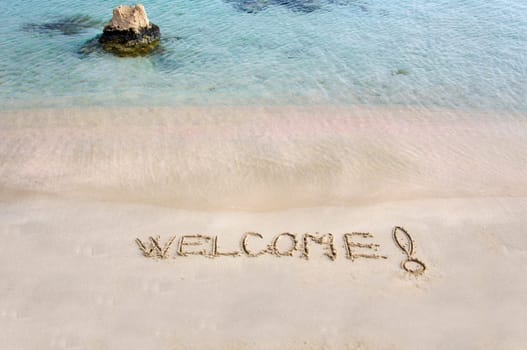 Welcome message written on white sand, with tropical sea waves in  background