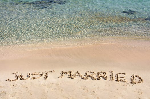 Just Married written in sand on a beautiful beach, blue clear waves in background