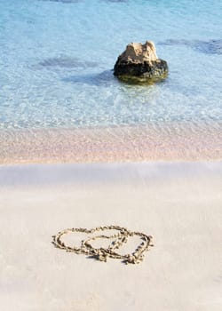 Two hearts drawn in the sand on a beautiful beach, with waves in background