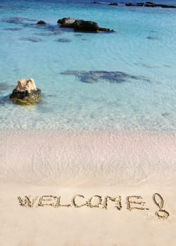 Welcome message written on white sand, with tropical sea waves in  background