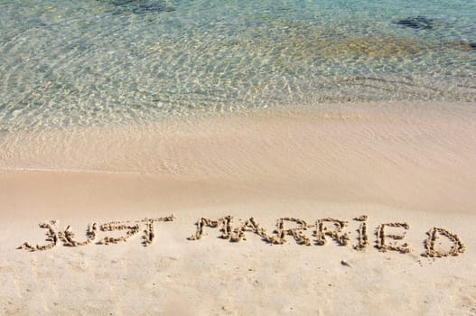 Just Married written in sand on a beautiful beach, blue clear waves in background