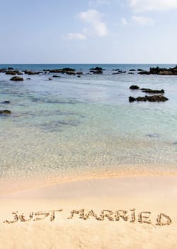 Just Married written in sand on a beautiful beach, blue clear waves in background