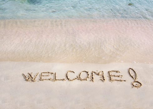 Welcome message written on white sand, with tropical sea waves in  background