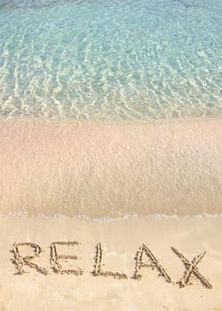 Relax word written in the sand, on a beautiful beach with clear blue waves in  background