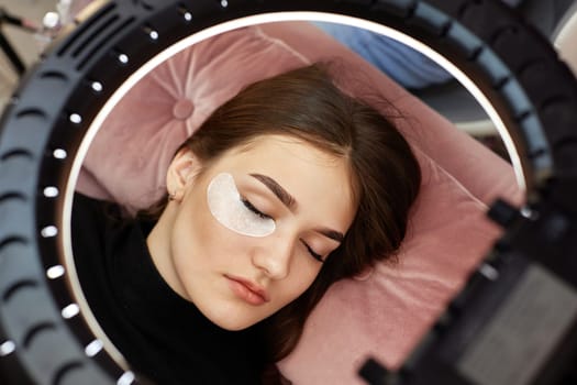 eyelash extension procedure. beautiful woman under ring light lamp, top view
