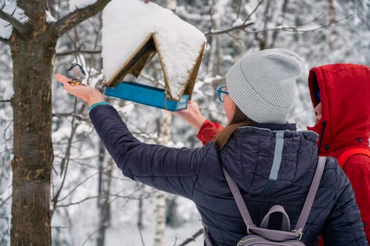 Woman in winter jacket feeding birds in snowy winter forest, snowy winter day.