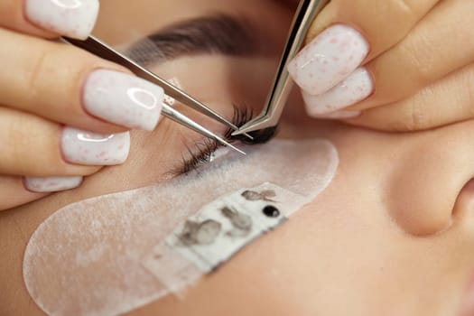 Beautiful female face during lash extension procedure in salon. Fake eyelashes