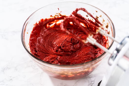 Mixing wet ingredients in a large glass mixing bowl to bake red velvet cupcakes with white chocolate ganache frosting.