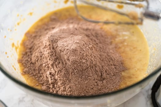 Mixing wet ingredients in a large glass mixing bowl to bake red velvet cupcakes with white chocolate ganache frosting.