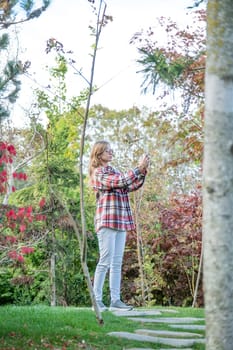 Woman in red plaid shirt enjoying nature standing in Japanese Garden taking photo on smartphone