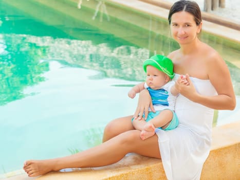 Baby and mother are sitting on the edge of a pool