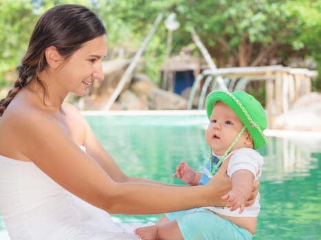 Baby and mother are sitting on the edge of a pool