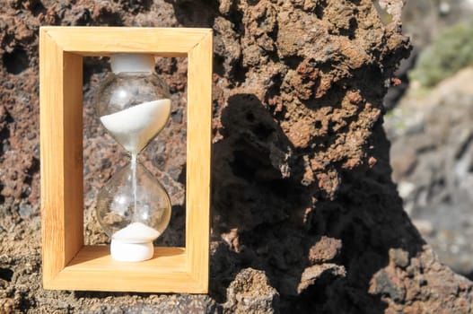 Time Concept White Sand Hourglass on the Volcanic Rocks