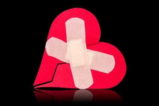 Broken heart with plaster. Isolated on black background