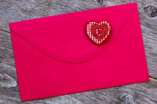 Red paper envelope with decorative heart, on the wooden background