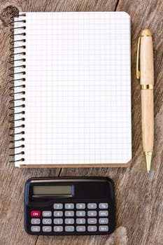 Adding up figures concept with calculator, pen and notebook on the wooden background
