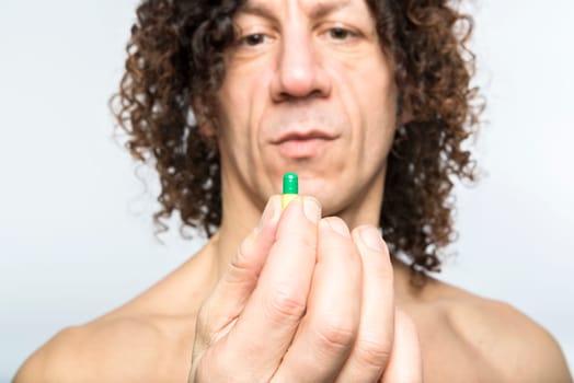 Cropped shot of bare chested mediterranean man holding colourful pill