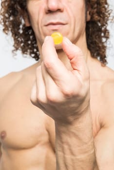 Cropped shot of bare chested mediterranean man holding colourful pill