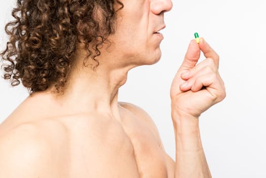 Cropped shot of bare chested mediterranean man taking colourful pill