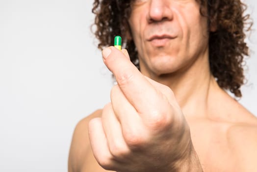 Cropped shot of bare chested mediterranean man holding colourful pill