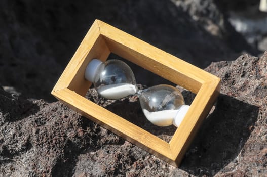 Time Concept White Sand Hourglass on the Volcanic Rocks