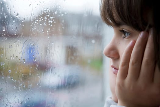 young child looking out of window on rainy day