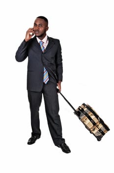 A black business man with his suitcase is standing for white background.in a blue suit and talking on the phone..