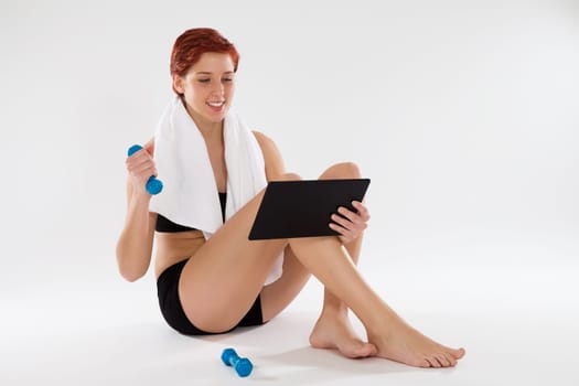 Young fitness woman with dumbbells receives fitness exercises from the Internet with her tablet PC