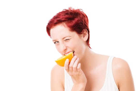 Young winking woman bites into an orange against a white background
