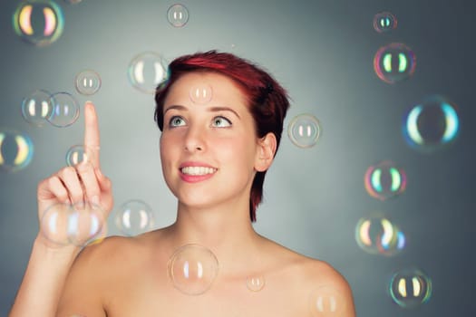 Young beautiful red-haired woman plays with colorful soap bubbles