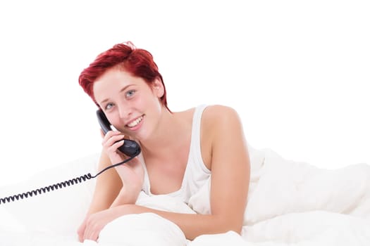 Young woman talking on the phone in bed in front of a white background
